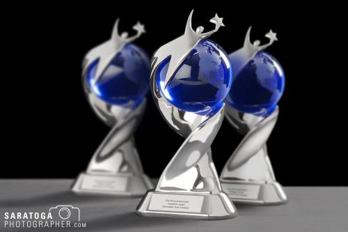 Three achievement awards swirling silver award holding blue glass globe on black background