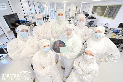Eight clean room lab technicians standing in a group facing camera all dressed in clean room bunny suits