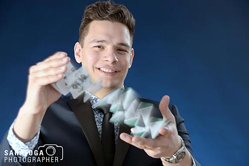 Young magician doing card trick on blue background