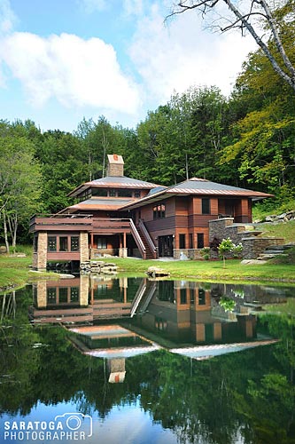 50s style vermont home reflected in water. featuing redwood siding and stone foundation