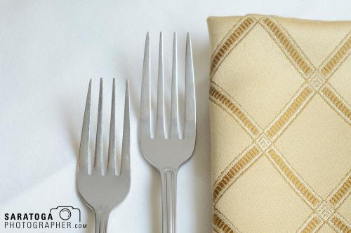 Salad and dinner forks next to napkin on white background