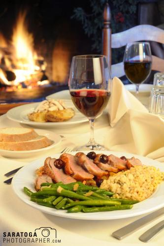 Fancy view of table setting with roaring fire and background and plate with asparagus risotto and pork in foreground with wine glass