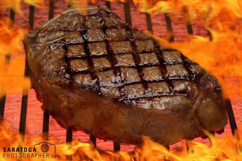 Steak cooking on flaming grill showing grill marks on top of meat