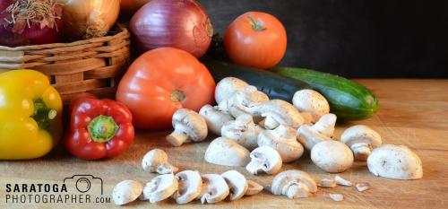 Low angle view of cutting board with sliced mushrooms In foreground and assorted vegetables and background