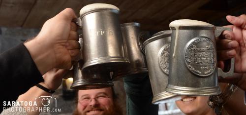 Close-up view of 6 pewter mugs filled with beer being raised in a toast