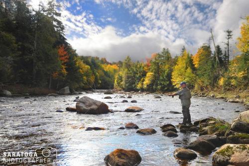 Fisherman casting with fly rod into Rocky stream on autumn day