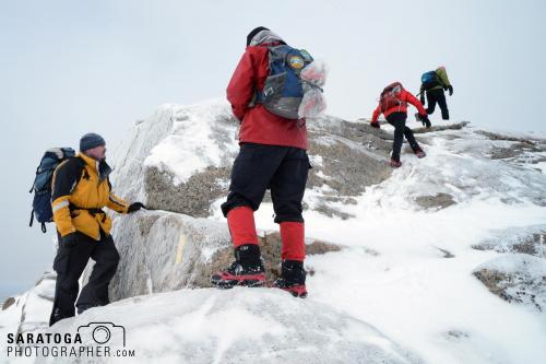 Four mountain climbers carrying packs reaching the summit of a peak in winter