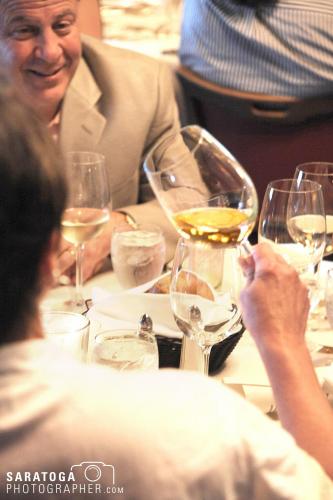 Looking over the shoulder of women holding wine glass at a table sitting and smiling man