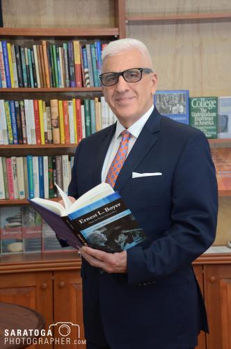 College professor in suit and tie holding book with library behind him