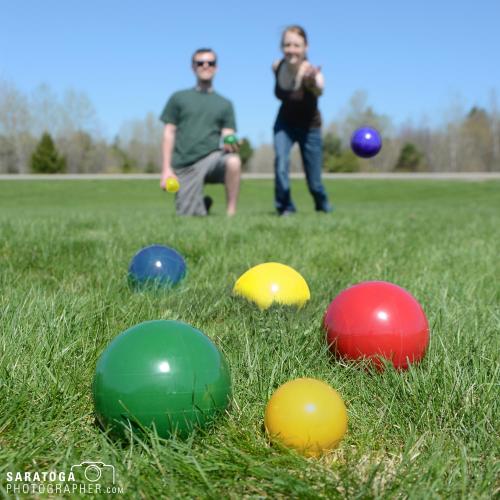 Multicolored lion sports heavy plastic bocce balls on grass with players out of focus and background