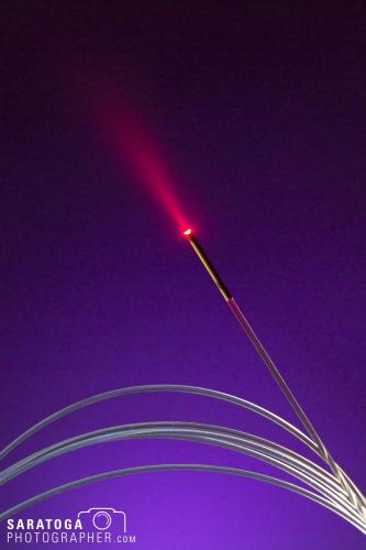 Glowing red end of fiber optic strand by AngioDynamics on graduated black to purple background