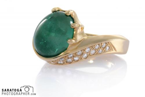 Heavy gold ring with emerald stone and insert diamonds on reflective white background